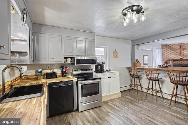 kitchen with sink, light hardwood / wood-style flooring, butcher block countertops, stainless steel appliances, and a wall unit AC