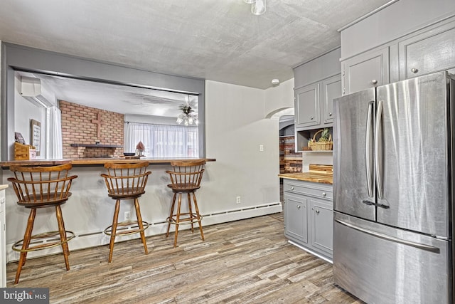 kitchen featuring a kitchen bar, stainless steel fridge, light wood-type flooring, and gray cabinetry