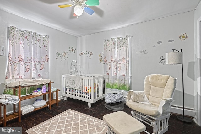 bedroom featuring ceiling fan, dark hardwood / wood-style flooring, a nursery area, and a baseboard radiator