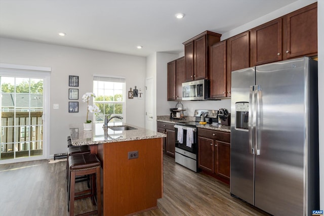 kitchen featuring a kitchen bar, a kitchen island with sink, sink, light stone counters, and stainless steel appliances