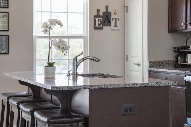 kitchen featuring a kitchen bar, light stone countertops, dark brown cabinetry, sink, and a kitchen island