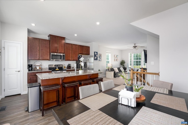 kitchen featuring a kitchen bar, appliances with stainless steel finishes, light stone counters, ceiling fan, and an island with sink