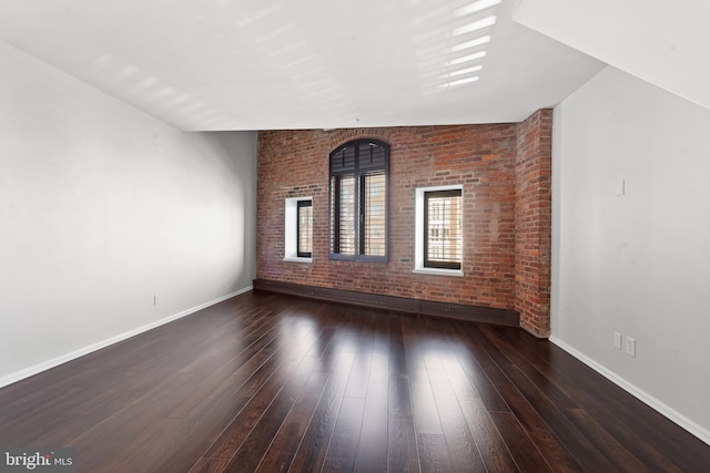 unfurnished room featuring dark hardwood / wood-style flooring, lofted ceiling, and brick wall