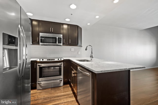 kitchen with kitchen peninsula, light stone countertops, stainless steel appliances, dark wood-type flooring, and sink