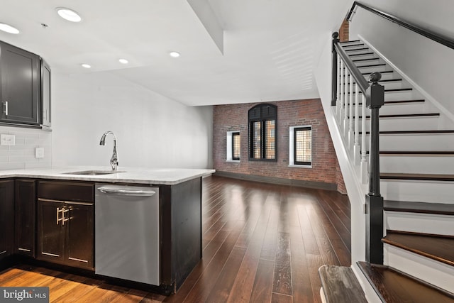 kitchen featuring dishwasher, sink, dark hardwood / wood-style floors, kitchen peninsula, and brick wall