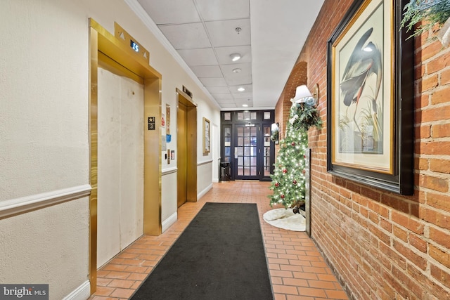 corridor with a drop ceiling, brick wall, and elevator