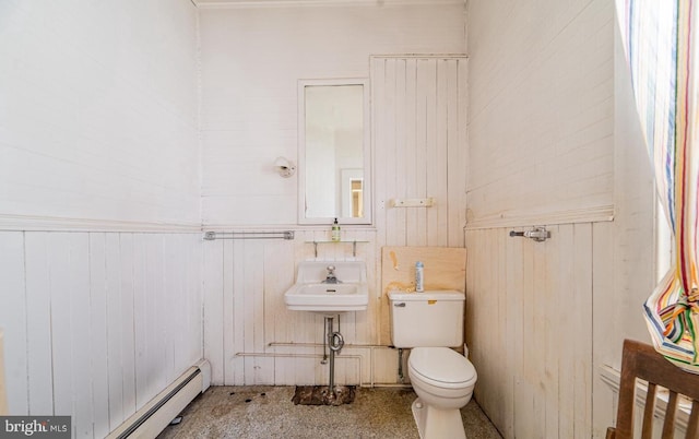 bathroom featuring baseboard heating, wood walls, sink, and toilet