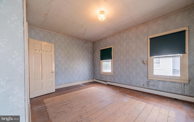 unfurnished room with hardwood / wood-style floors, a wealth of natural light, and a baseboard heating unit