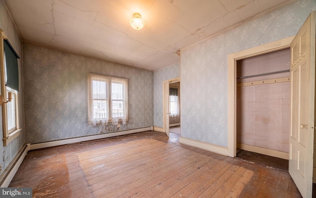 unfurnished bedroom featuring hardwood / wood-style floors, a closet, and a baseboard radiator