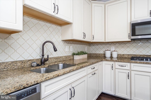 kitchen with decorative backsplash, light stone counters, stainless steel appliances, sink, and white cabinets