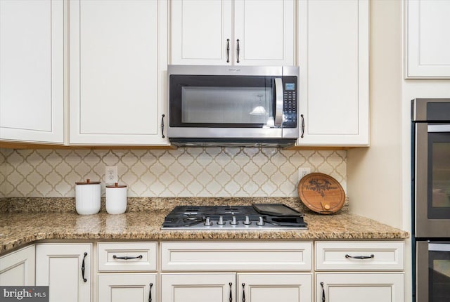 kitchen featuring light stone countertops, backsplash, stainless steel appliances, and white cabinetry