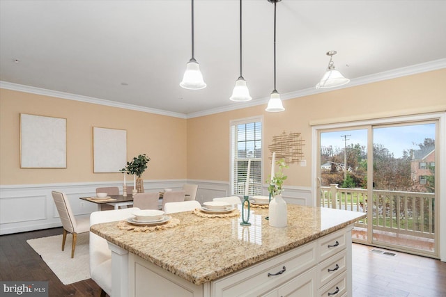 kitchen featuring a center island, white cabinets, crown molding, decorative light fixtures, and light stone counters