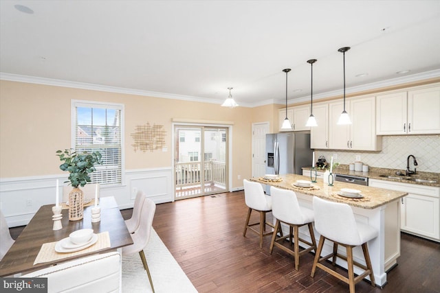 kitchen featuring a kitchen island with sink, sink, appliances with stainless steel finishes, decorative light fixtures, and light stone counters