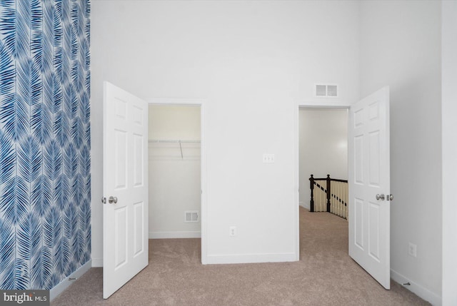 unfurnished bedroom with light carpet, a high ceiling, a spacious closet, and a closet