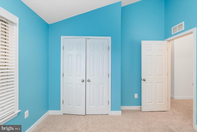 unfurnished bedroom featuring a closet, light colored carpet, and vaulted ceiling