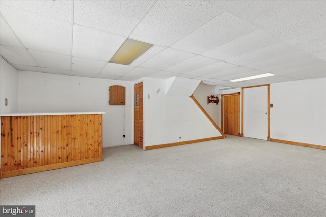 interior space with a paneled ceiling, wood walls, and light colored carpet