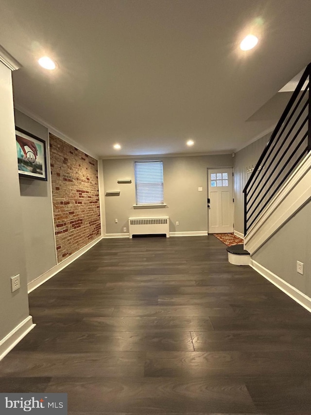 interior space with dark hardwood / wood-style floors, radiator heating unit, ornamental molding, and brick wall