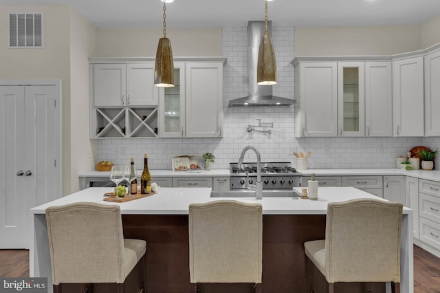 kitchen featuring backsplash, a kitchen breakfast bar, wall chimney exhaust hood, and a center island with sink