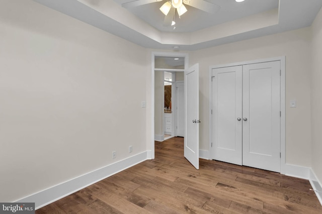 unfurnished bedroom featuring a raised ceiling, light wood-type flooring, ceiling fan, and a closet