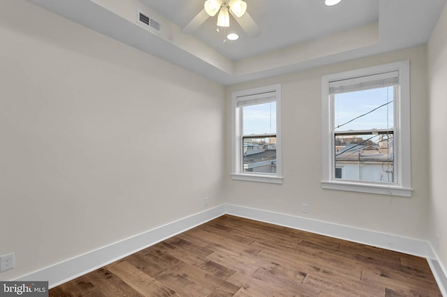 empty room with hardwood / wood-style flooring, ceiling fan, and a tray ceiling