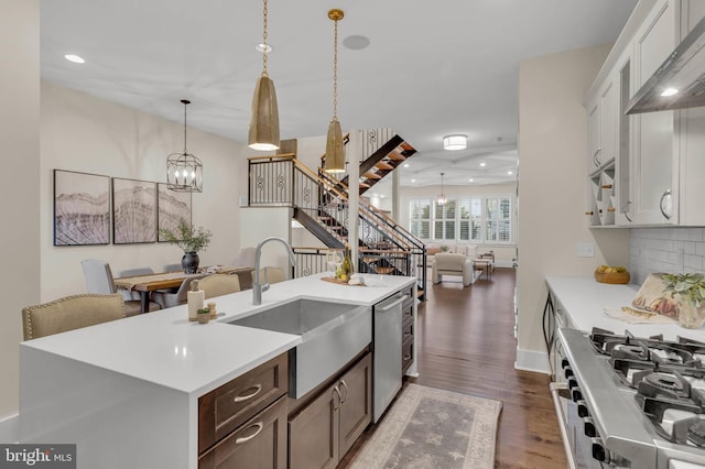 kitchen with appliances with stainless steel finishes, white cabinetry, sink, hanging light fixtures, and a center island with sink