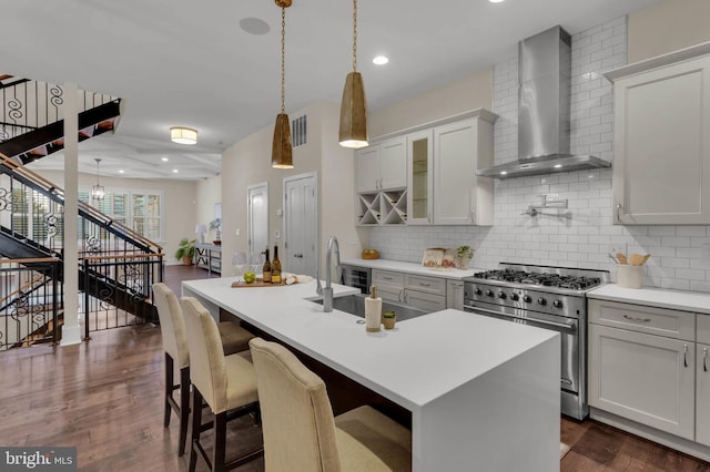 kitchen with decorative light fixtures, an island with sink, decorative backsplash, high end stainless steel range oven, and wall chimney exhaust hood