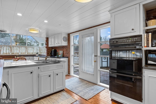 kitchen with white cabinetry, black double oven, sink, and light wood-type flooring