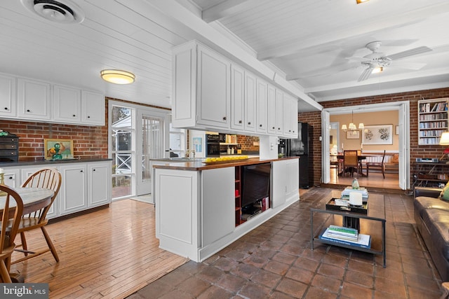 kitchen featuring white cabinetry, dark hardwood / wood-style floors, brick wall, ceiling fan with notable chandelier, and beamed ceiling