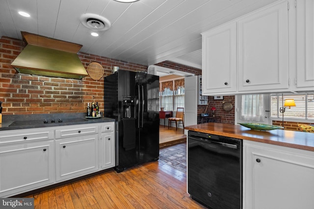 kitchen with premium range hood, white cabinetry, light wood-type flooring, brick wall, and black appliances