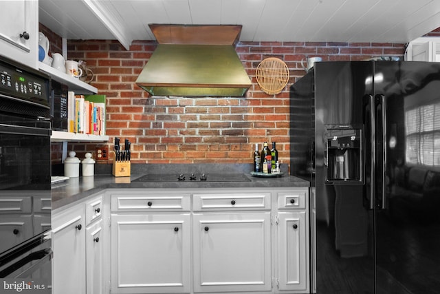 kitchen featuring premium range hood, brick wall, white cabinets, and black appliances