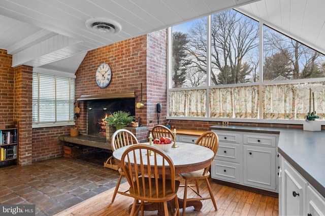 dining space with vaulted ceiling with beams, a fireplace, wood-type flooring, and brick wall