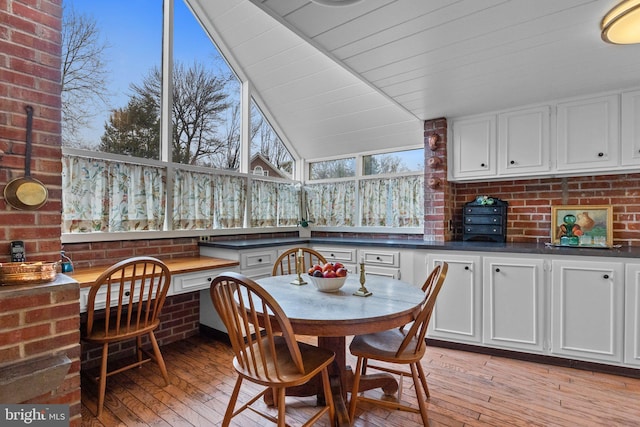 dining area with lofted ceiling, light hardwood / wood-style flooring, built in desk, brick wall, and wooden ceiling