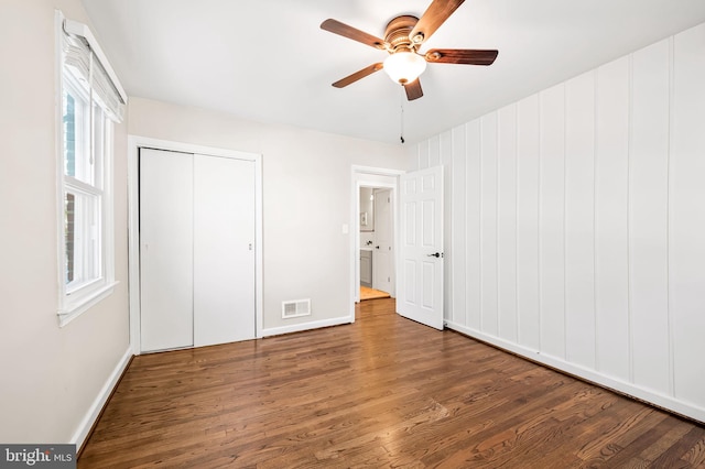 unfurnished bedroom with ceiling fan, multiple windows, dark hardwood / wood-style flooring, and a closet