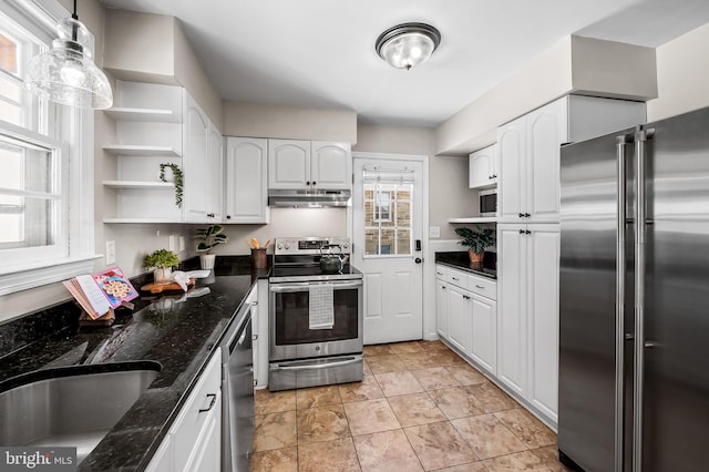 kitchen with white cabinetry, stainless steel appliances, dark stone countertops, pendant lighting, and sink