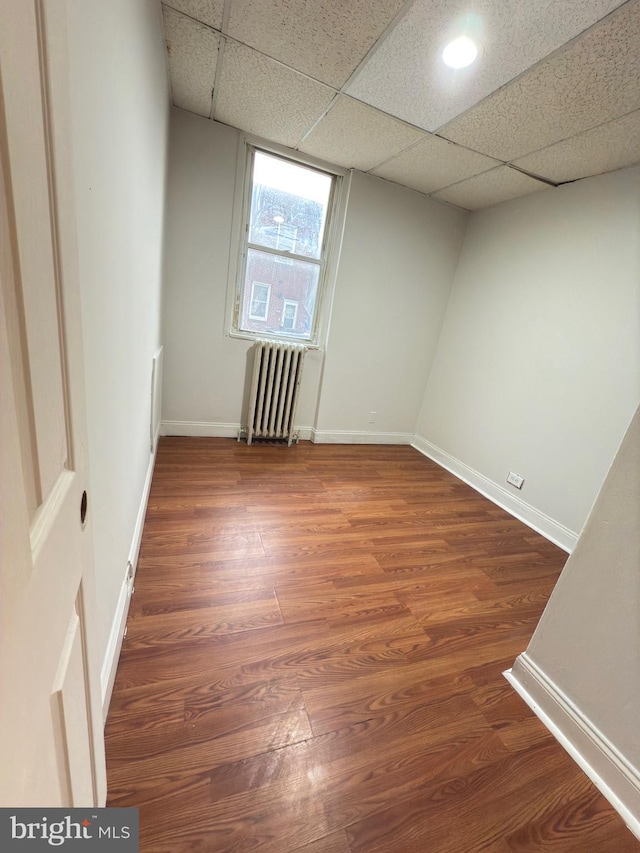 unfurnished room with a paneled ceiling, radiator heating unit, and dark wood-type flooring