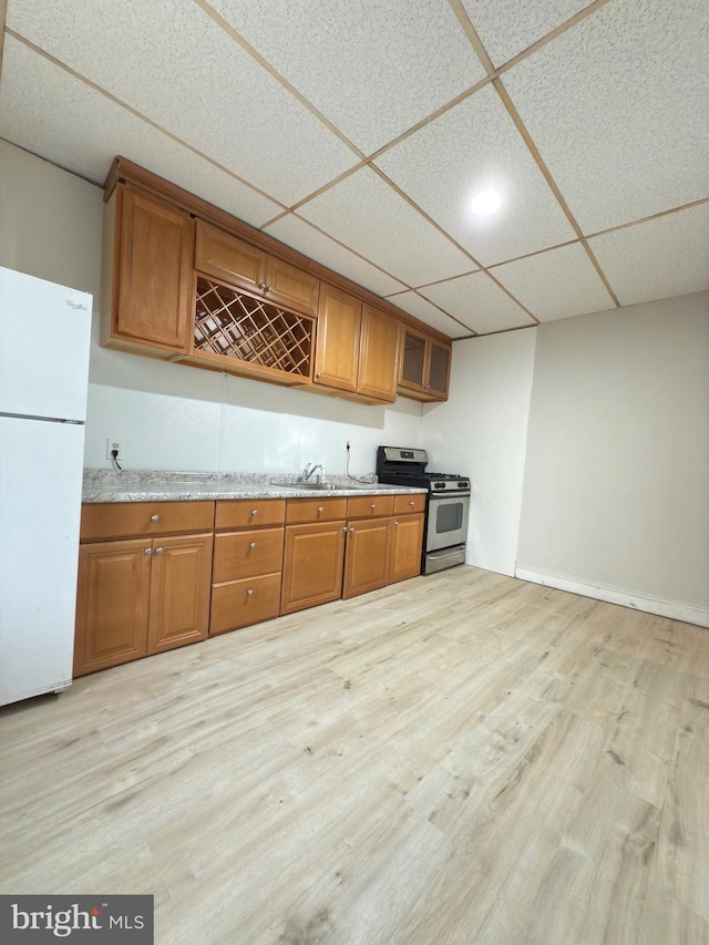 kitchen featuring sink, stainless steel range with gas cooktop, white refrigerator, light hardwood / wood-style floors, and a paneled ceiling