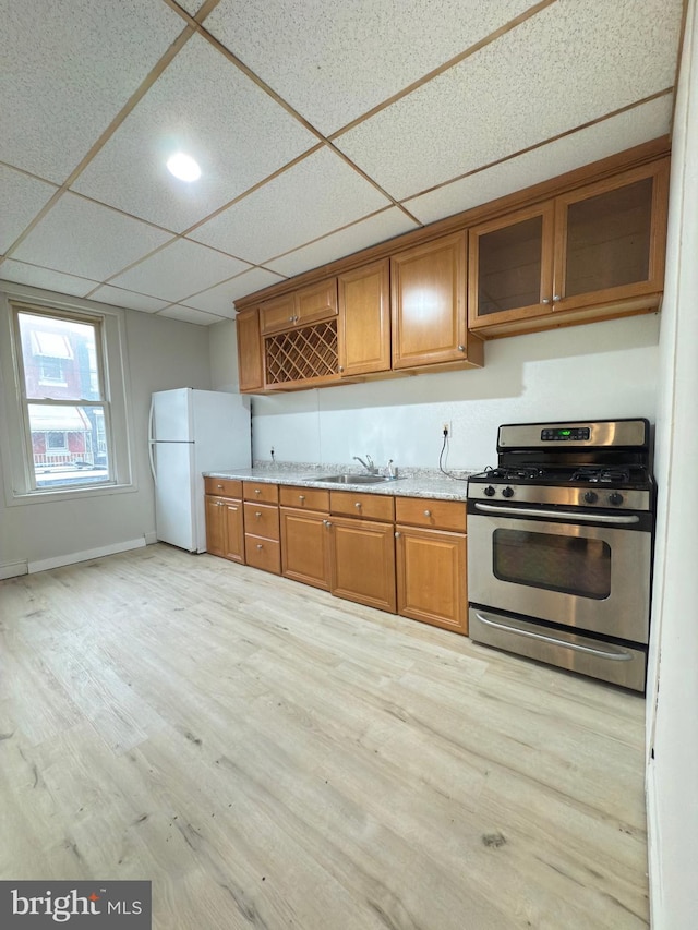 kitchen featuring light wood-type flooring, a paneled ceiling, gas stove, sink, and white fridge