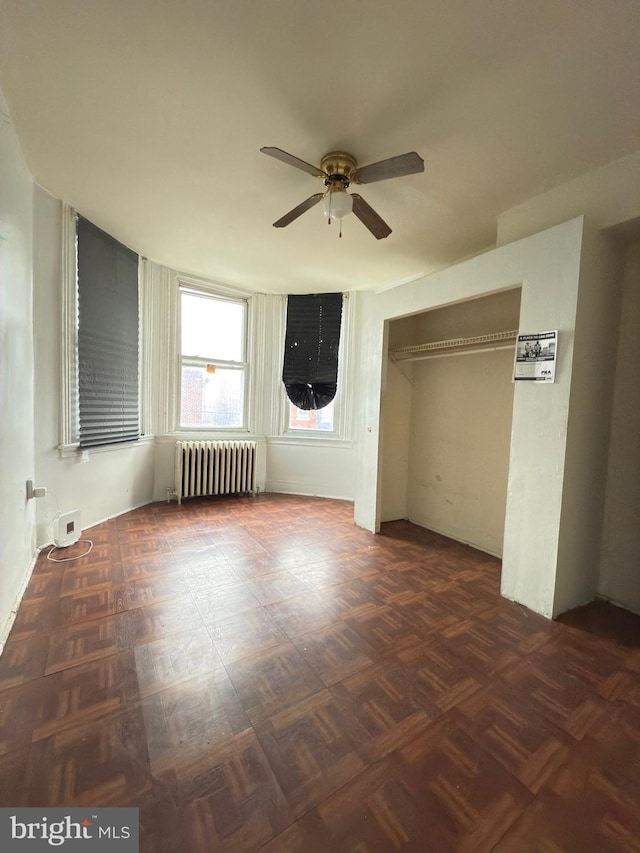 unfurnished room featuring ceiling fan, dark parquet flooring, and radiator