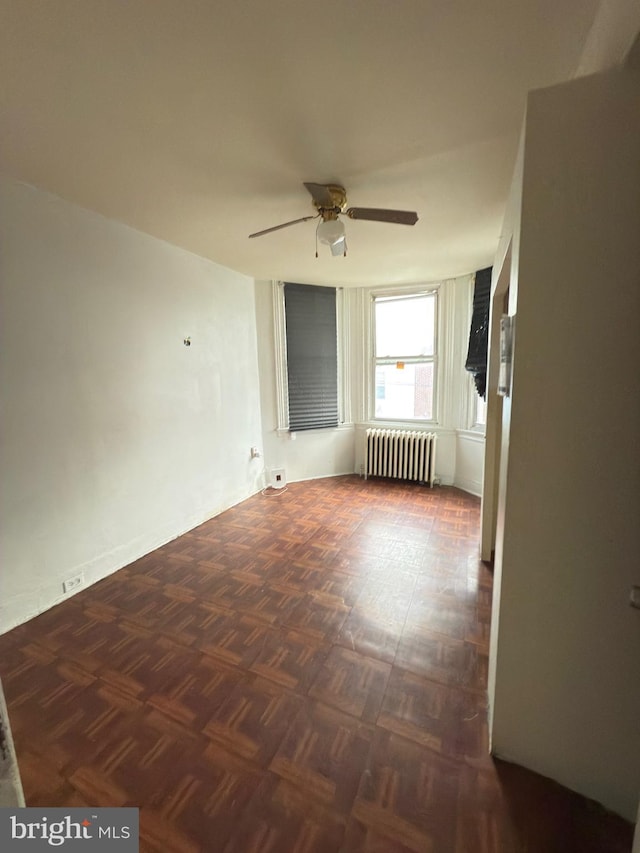 spare room featuring radiator, ceiling fan, and dark parquet floors