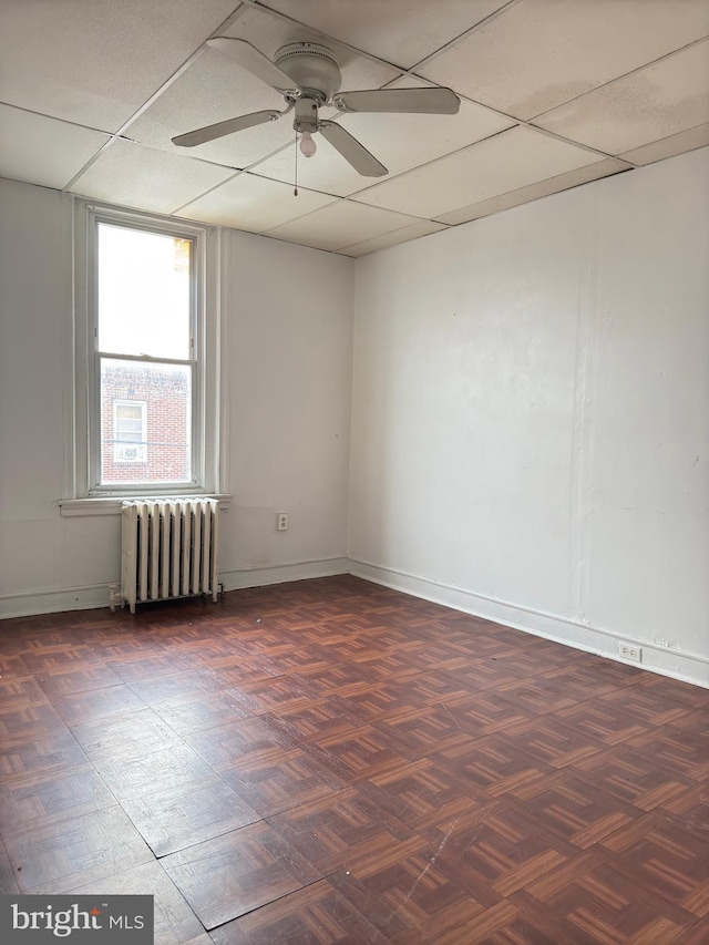 unfurnished room with radiator heating unit, dark parquet floors, ceiling fan, and a paneled ceiling