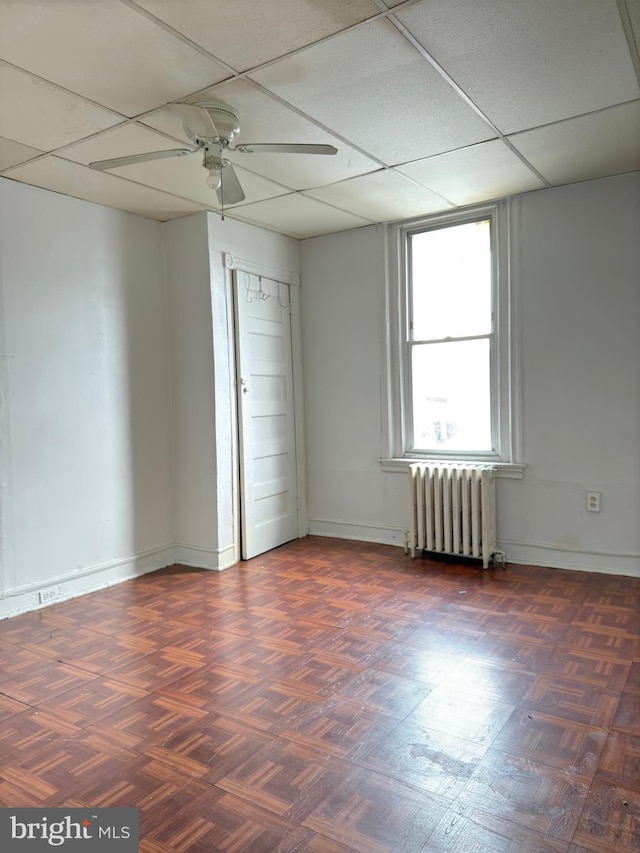 unfurnished room with a paneled ceiling, ceiling fan, radiator heating unit, and dark parquet floors