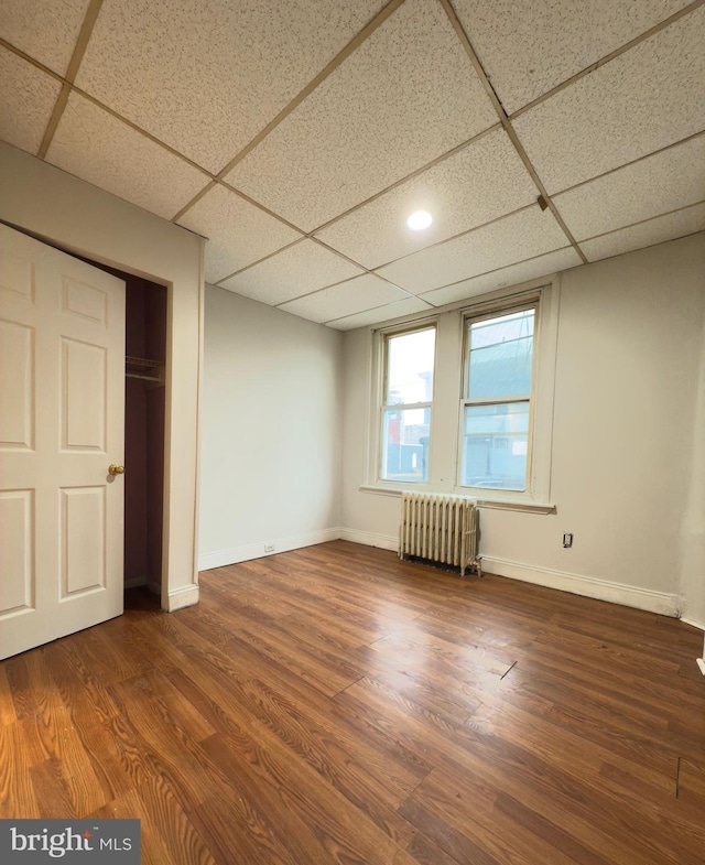 unfurnished bedroom with radiator, a closet, a drop ceiling, and dark hardwood / wood-style floors