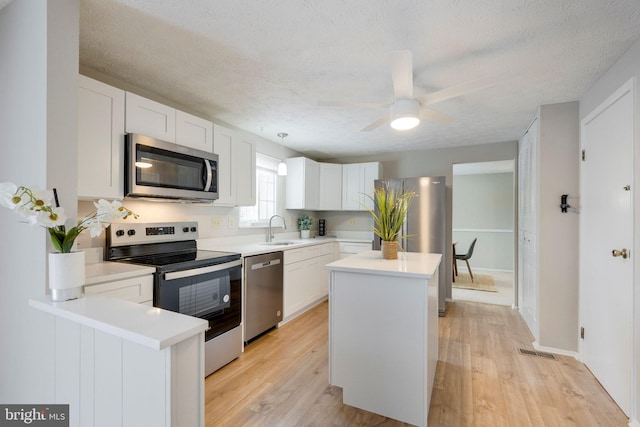 kitchen with decorative light fixtures, white cabinetry, sink, stainless steel appliances, and a textured ceiling