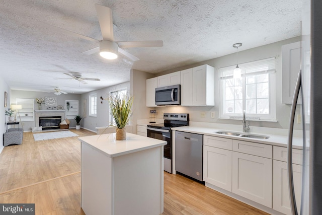 kitchen featuring appliances with stainless steel finishes, white cabinetry, sink, hanging light fixtures, and light wood-type flooring