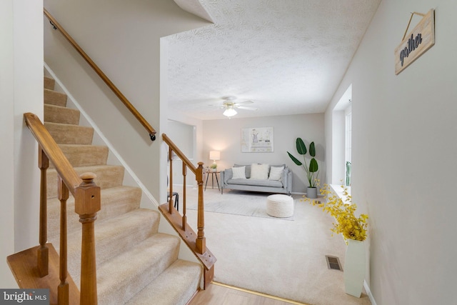 living room featuring a textured ceiling, ceiling fan, visible vents, baseboards, and stairs