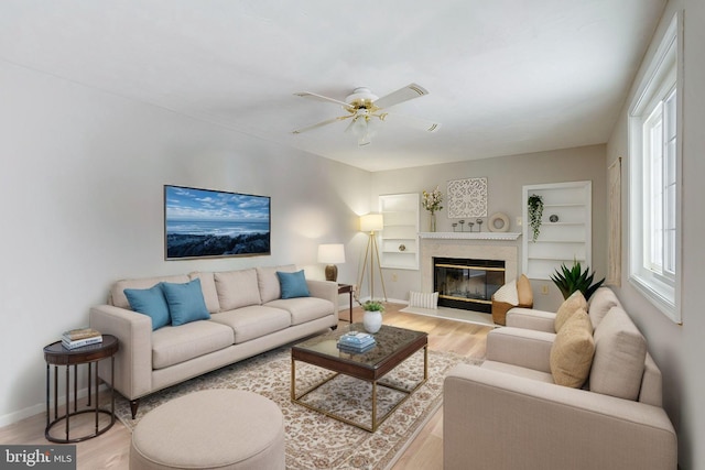 living room with built in shelves, light hardwood / wood-style floors, a premium fireplace, and ceiling fan