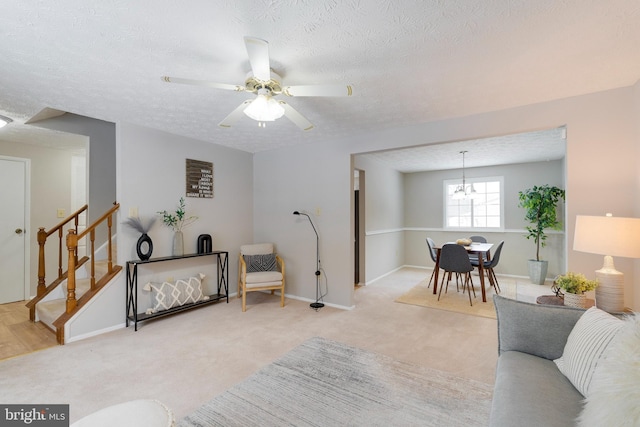 living room featuring carpet floors, stairs, a textured ceiling, baseboards, and ceiling fan with notable chandelier