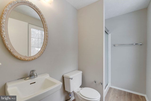 bathroom with toilet, sink, a textured ceiling, a shower with door, and hardwood / wood-style floors