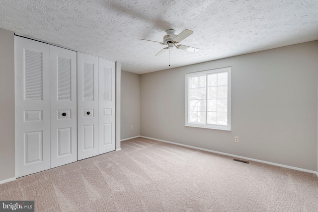 unfurnished bedroom with ceiling fan, light colored carpet, a closet, and a textured ceiling