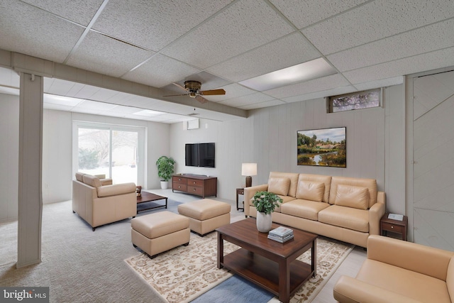 living room with a paneled ceiling, light colored carpet, ceiling fan, and wood walls